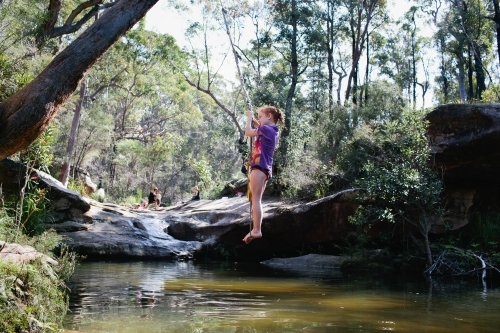 Young girl swinging on a rope swing at a waterhole - Australian Stock Image