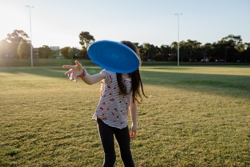 Young girl throwing a flying disk / frisbee at a sports field (oval) at sunset