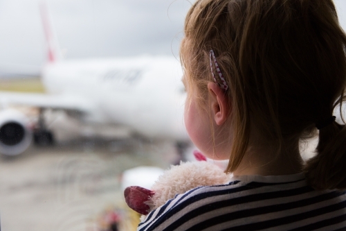 Young girl waiting for a flight, looking out a window while holding a toy cat