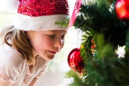 young girl wearing a santa hat smiling with a christmas tree