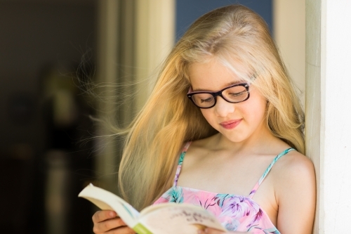 Young girl wearing glasses reading a book - Australian Stock Image