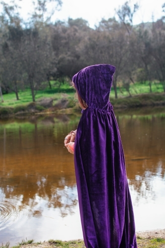 Young girl with a purple cape playing by river