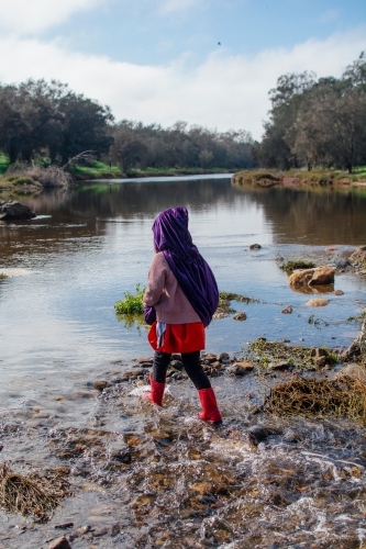 Young girl with a purple cape playing by river - Australian Stock Image