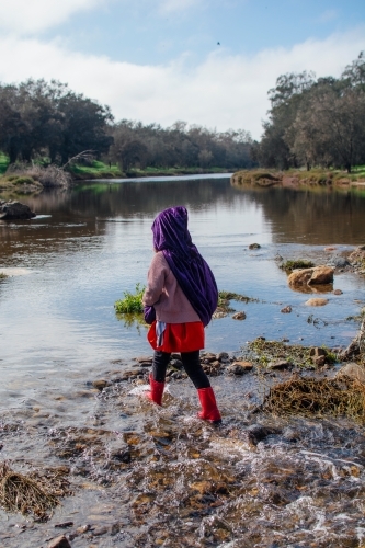 Young girl with a purple cape playing by river