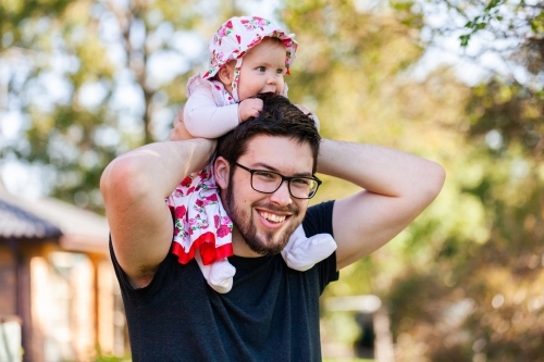 Young girl with hat on outside riding on her fathers shoulders - Australian Stock Image
