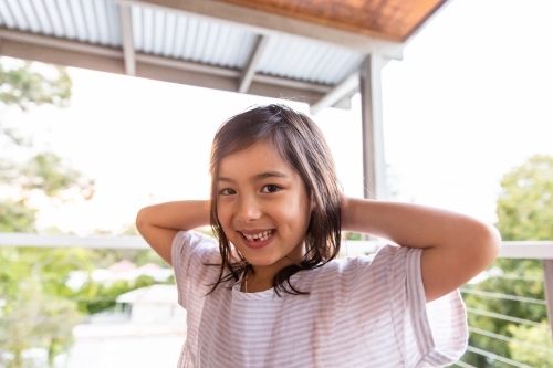 Young girl with her hands at the back of her head smiling - Australian Stock Image