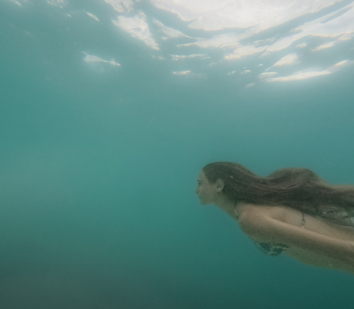 Young Girl with long hair swimming through green ocean water taken underwater - Australian Stock Image
