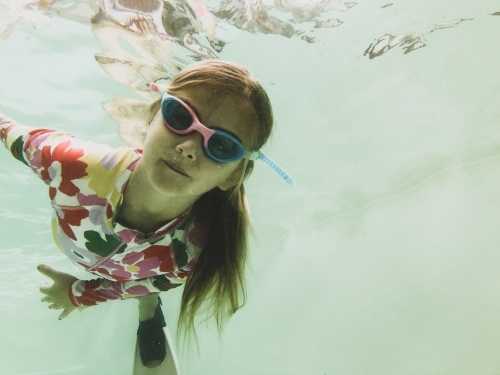 Young girls swimming underwater in pool wearing floral swimsuit, goggles and fins