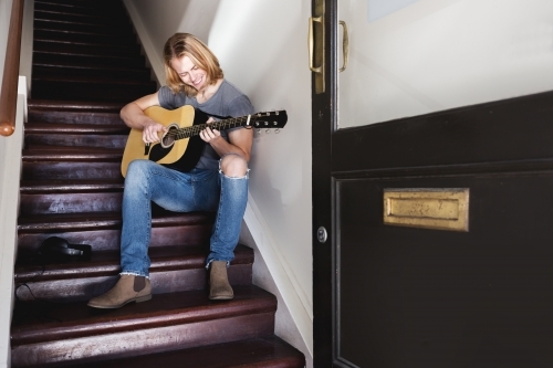 Young guy smiling playing guitar in a stairway - Australian Stock Image