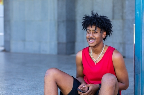 young guy with smartphone wearing red athletic singlet - Australian Stock Image
