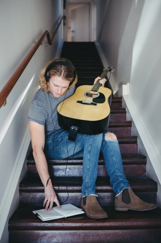 Young guy writing music on a staircase - Australian Stock Image
