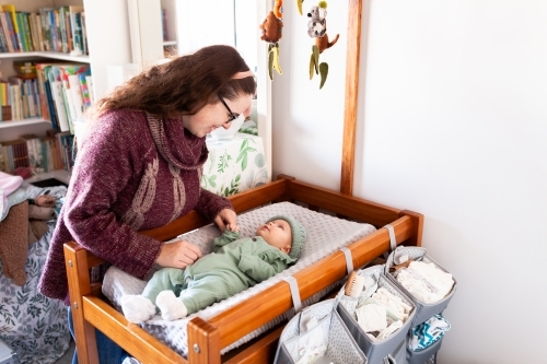 Young happy mum getting baby dressed for winter on change table in nursery