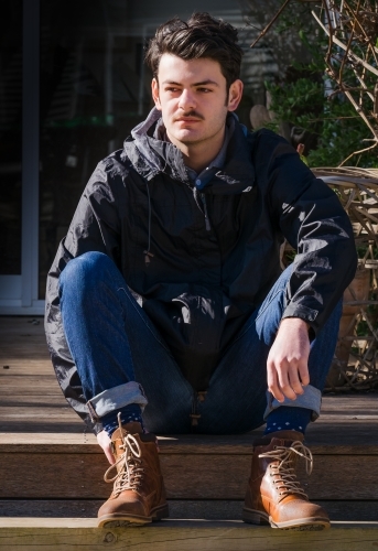 Young hip man sitting in the morning sun. - Australian Stock Image