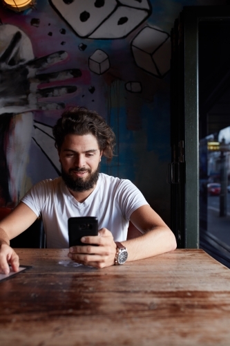 Young hipster man checking mobile phone at bar - Australian Stock Image