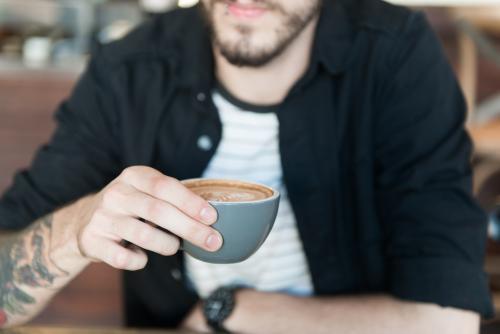 Young hipster man drinking coffee in a modern cafe - Australian Stock Image