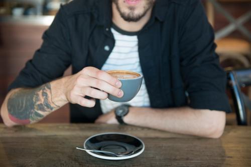 Young hipster man drinking coffee in a modern cafe - Australian Stock Image