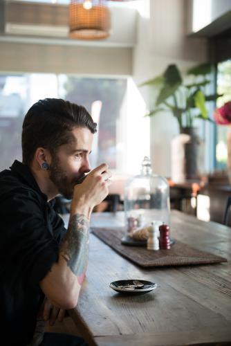 Young hipster man drinking coffee in a modern cafe - Australian Stock Image
