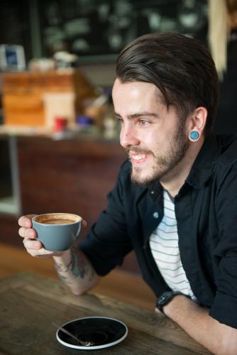 Young hipster man drinking coffee in a modern cafe - Australian Stock Image