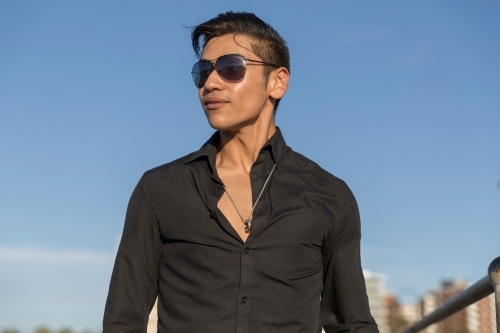 Young hispanic male in black shirt and sunglasses with blue sky backdrop