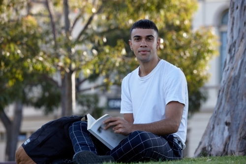 Young Indigenous Australian man enjoying  reading time outdoors - Australian Stock Image