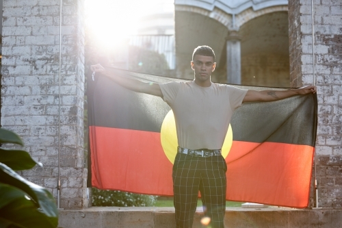 Young Indigenous Australian man holding Aboriginal flag - Australian Stock Image