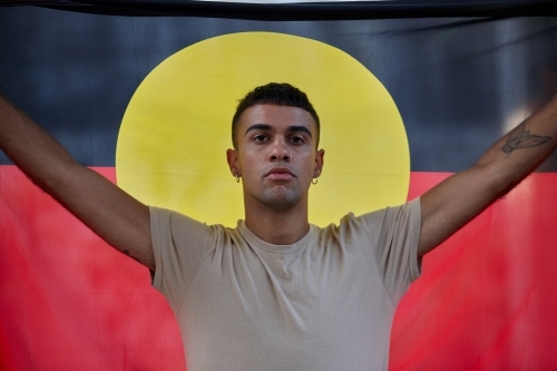 Young Indigenous Australian man holding Aboriginal flag - Australian Stock Image
