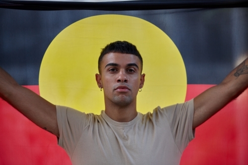 Young Indigenous Australian man holding Aboriginal flag - Australian Stock Image