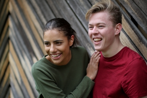 Young interracial couple laughing together in front of textured wooden panels - Australian Stock Image