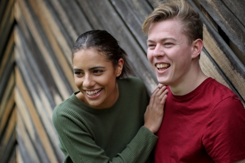 Young interracial couple laughing together in front of textured wooden panels