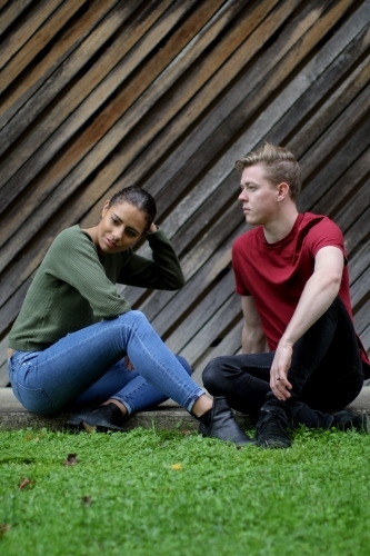 Young interracial couple sitting on the ground and having a tense conversation