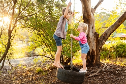 Young kids playing together on tire swing in backyard - Australian Stock Image
