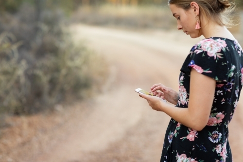 young lady in rural setting looking at her mobile phone - Australian Stock Image