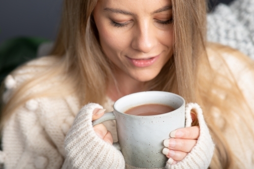 Young lady relaxing drinking hot chocolate or coffee on a cold winters day - Australian Stock Image