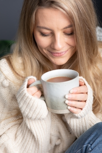 Young lady relaxing drinking hot chocolate or coffee on a cold winters day - Australian Stock Image