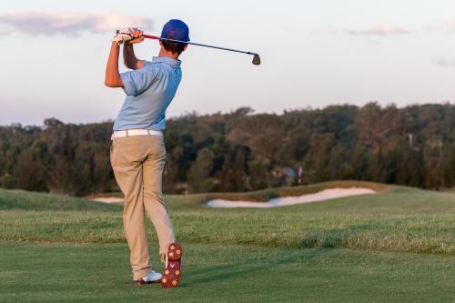 Young male golfer watching approach shot from behind