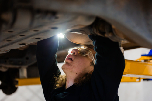 Young male mechanic working on the vehicles underbody with flashlight on - Australian Stock Image