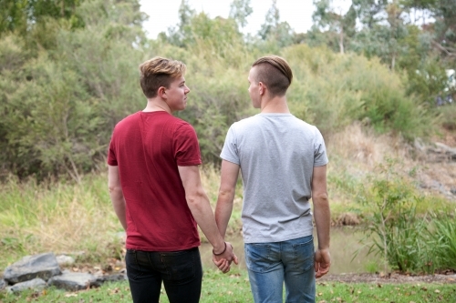 Young male same sex couple holding hands in a rural setting - Australian Stock Image