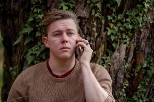 Young male sitting outside using mobile phone - Australian Stock Image