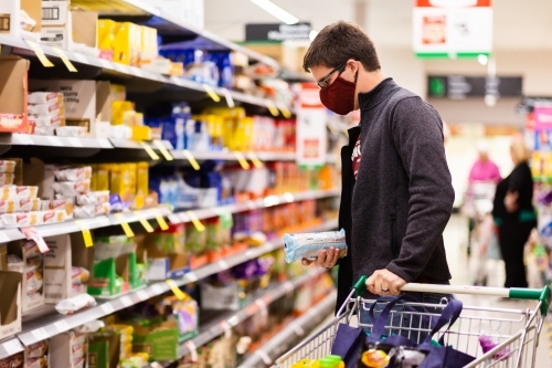 Young man doing grocery shopping for family during coronavirus outbreak wearing a face mask - Australian Stock Image