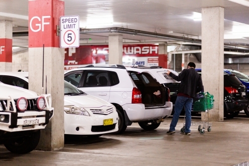 Young man doing the shopping and taking re-usable bags of groceries to the car - Australian Stock Image