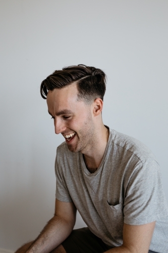 Young man laughing grey shirt plain background - Australian Stock Image