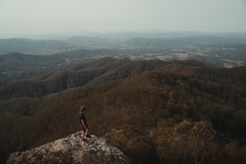 Young man on a mountain top looking at the views of the valley below. - Australian Stock Image