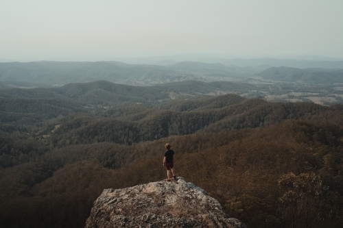 Young man on a mountain top looking at the views of the valley below. - Australian Stock Image
