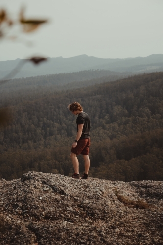 Young man on a mountain top looking at the views of the valley below. - Australian Stock Image