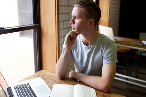 Young man sitting at a desk in a classroom looking out the window - Australian Stock Image