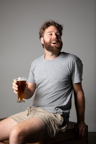 Young man sitting, holding a glass of beer, relaxed and happy