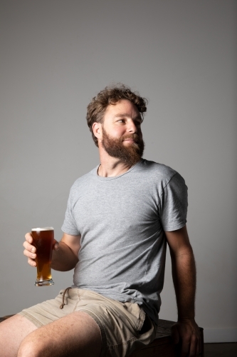 Young man sitting, holding a glass of beer, relaxed and happy
