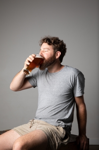 Young man sitting, holding a glass of beer, relaxed and happy