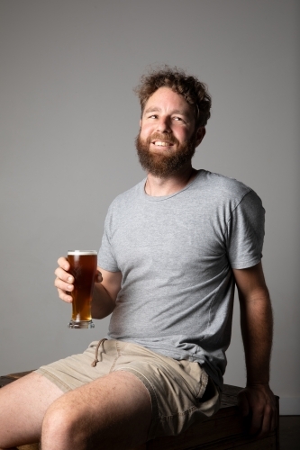 Young man sitting, holding a glass of beer, relaxed and happy