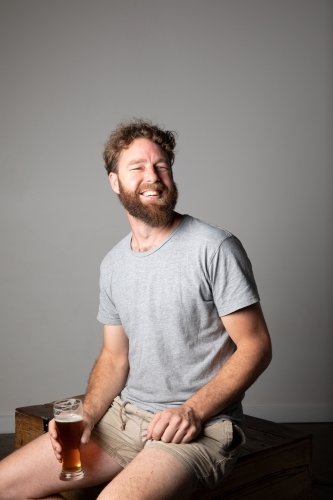 Young man sitting, holding a glass of beer, relaxed and happy